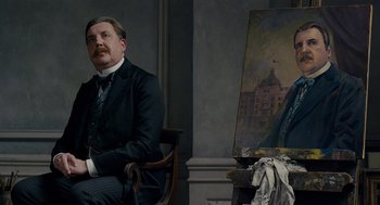 Movie still from “The Danish Girl” (2015), directed by Tom Hooper – A man sitting in front of an easel in front of a painting; Medium shot, Low angle