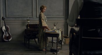 Movie still from “The Danish Girl” (2015), directed by Tom Hooper – A woman standing in front of a table in a room; Wide shot, High angle