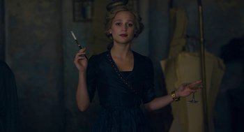 Movie still from “The Danish Girl” (2015), directed by Tom Hooper – A woman holding a knife in her hand and wearing a black dress; Medium shot, Over the shoulder angle