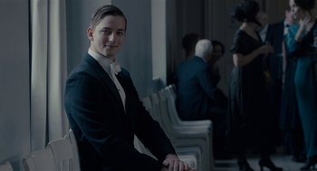 Movie still from “The Danish Girl” (2015), directed by Tom Hooper – A man in a suit sitting in a row of white chairs; Medium shot, Over the shoulder angle
