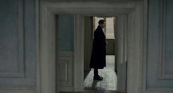 Movie still from “The Danish Girl” (2015), directed by Tom Hooper – A man in a long coat standing in a doorway; Wide shot, High angle