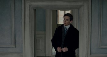Movie still from “The Danish Girl” (2015), directed by Tom Hooper – A man in a suit and tie standing in front of an open door; Medium shot, Over the shoulder angle