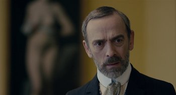 Movie still from “The Danish Girl” (2015), directed by Tom Hooper – An older man in a suit and tie looking at the camera; Close Up shot, Over the shoulder angle