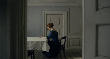 Movie still from “The Danish Girl” (2015), directed by Tom Hooper – A woman sitting at a dining room table writing; Wide shot, Over the shoulder angle