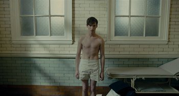 Movie still from “The Danish Girl” (2015), directed by Tom Hooper – A shirtless man standing in front of a window; Medium shot, Low angle