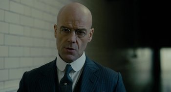 Movie still from “The Danish Girl” (2015), directed by Tom Hooper – A bald man in a suit and tie looking at the camera; Close Up shot, Low angle