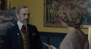 Movie still from “The Danish Girl” (2015), directed by Tom Hooper – An older man in a suit and tie talking to an older woman; Medium shot, Over the shoulder angle