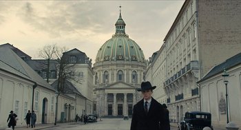 Movie still from “The Danish Girl” (2015), directed by Tom Hooper – A man in a hat and a suit stands in front of a building; Extreme Wide shot, Low angle