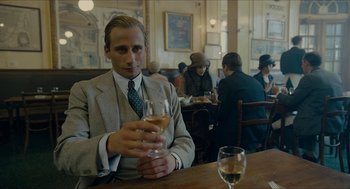 Movie still from “The Danish Girl” (2015), directed by Tom Hooper – A man sitting at a table holding a glass of wine; Medium shot, Over the shoulder angle
