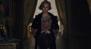 Movie still from “The Danish Girl” (2015), directed by Tom Hooper – A woman holding a hat in a room with curtains; Medium shot, Over the shoulder angle