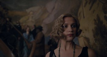 Movie still from “The Danish Girl” (2015), directed by Tom Hooper – A woman in a black dress and a green necklace; Close Up shot, Over the shoulder angle