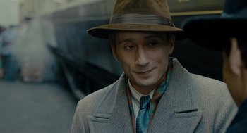 Movie still from “The Danish Girl” (2015), directed by Tom Hooper – A man wearing a hat and a coat and a tie; Close Up shot, Over the shoulder angle