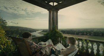 Movie still from “The Danish Girl” (2015), directed by Tom Hooper – Two women sitting on a bench near a river; Wide shot, High angle