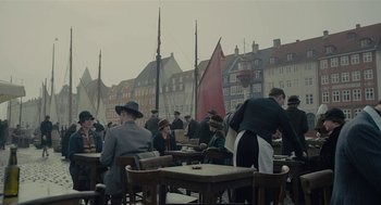 Movie still from “The Danish Girl” (2015), directed by Tom Hooper – A group of people sitting at a table with chairs; Wide shot, High angle