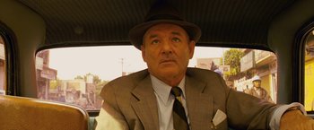 Movie still from “The Darjeeling Limited” (2007), directed by Wes Anderson – A man wearing a suit and hat sitting in a car; Close Up shot, Low angle
