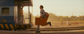 Movie still from “The Darjeeling Limited” (2007), directed by Wes Anderson – A man is running with a suitcase on his back; Wide shot, Low angle