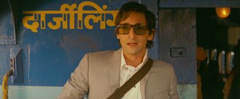 Movie still from “The Darjeeling Limited” (2007), directed by Wes Anderson – A man in a suit and sunglasses is posing for a picture; Close Up shot, Low angle