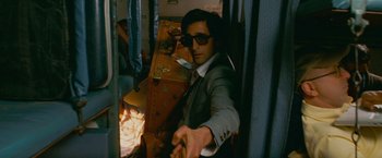Movie still from “The Darjeeling Limited” (2007), directed by Wes Anderson – A man in a suit and sunglasses sitting in a chair; Medium shot, High angle