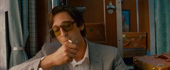 Movie still from “The Darjeeling Limited” (2007), directed by Wes Anderson – A man in a suit and sunglasses smoking a cigarette; Close Up shot, Low angle