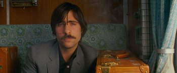 Movie still from “The Darjeeling Limited” (2007), directed by Wes Anderson – A man sitting in front of a wooden table; Close Up shot, Low angle