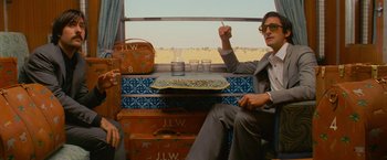 Movie still from “The Darjeeling Limited” (2007), directed by Wes Anderson – A man sitting on top of a train next to another man; Medium shot, Low angle