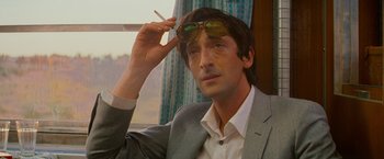 Movie still from “The Darjeeling Limited” (2007), directed by Wes Anderson – A man in a suit and sunglasses smoking a cigarette in front of a window; Close Up shot, Low angle