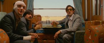 Movie still from “The Darjeeling Limited” (2007), directed by Wes Anderson – Two men sitting on a train with drinks and cigarettes; Medium shot, Low angle