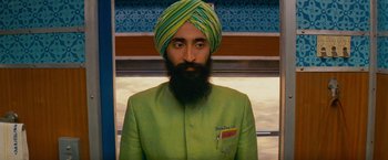 Movie still from “The Darjeeling Limited” (2007), directed by Wes Anderson – A man with a beard wearing a turban and a green suit; Medium shot, Over the shoulder angle