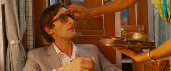 Movie still from “The Darjeeling Limited” (2007), directed by Wes Anderson – A man in a suit getting his sunglasses adjusted by a woman; Close Up shot, Over the shoulder angle