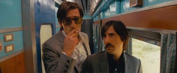 Movie still from “The Darjeeling Limited” (2007), directed by Wes Anderson – A man smoking a cigarette next to another man in a suit; Medium shot, Low angle