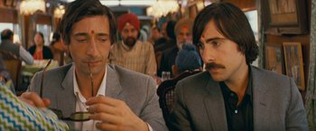 Movie still from “The Darjeeling Limited” (2007), directed by Wes Anderson – Two men sitting at a table in front of other people; Close Up shot, Over the shoulder angle