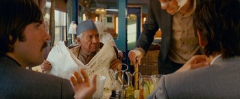 Movie still from “The Darjeeling Limited” (2007), directed by Wes Anderson – An old man sitting at a table reading a newspaper; Medium shot, Over the shoulder angle