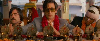 Movie still from “The Darjeeling Limited” (2007), directed by Wes Anderson – A man in a suit sitting in front of candles; Medium shot, Low angle
