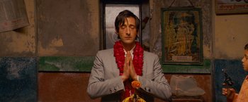 Movie still from “The Darjeeling Limited” (2007), directed by Wes Anderson – A man in a gray suit and a red flower lei; Medium shot, Low angle