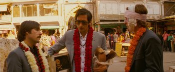 Movie still from “The Darjeeling Limited” (2007), directed by Wes Anderson – A man in a gray suit holding a bag of food; Medium shot, Low angle