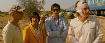 Movie still from “The Darjeeling Limited” (2007), directed by Wes Anderson – A man standing next to a group of people; Medium shot, Low angle