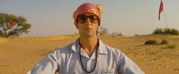 Movie still from “The Darjeeling Limited” (2007), directed by Wes Anderson – A man wearing a pink hat and sunglasses in the desert; Close Up shot, Low angle