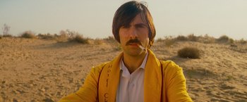 Movie still from “The Darjeeling Limited” (2007), directed by Wes Anderson – A man in a yellow jacket smoking a cigarette in the desert; Close Up shot, Low angle