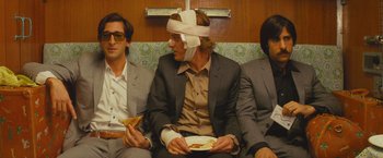Movie still from “The Darjeeling Limited” (2007), directed by Wes Anderson – A group of men sitting next to each other on a couch; Medium shot, Low angle