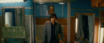 Movie still from “The Darjeeling Limited” (2007), directed by Wes Anderson – A man in a suit standing in front of a painting; Medium shot, Over the shoulder angle