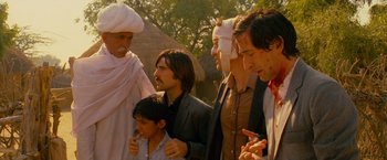 Movie still from “The Darjeeling Limited” (2007), directed by Wes Anderson – A group of men standing around a young boy; Medium shot, Over the shoulder angle