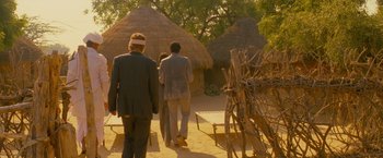 Movie still from “The Darjeeling Limited” (2007), directed by Wes Anderson – Three people are walking down a path in front of some huts; Wide shot, Over the shoulder angle