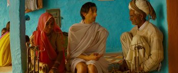 Movie still from “The Darjeeling Limited” (2007), directed by Wes Anderson – A man sitting on the ground wearing a white robe; Medium shot, Low angle