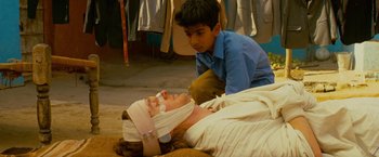 Movie still from “The Darjeeling Limited” (2007), directed by Wes Anderson – A man is laying on the ground with bandages on his head and a boy is kneeling over him; Medium shot, Over the shoulder angle