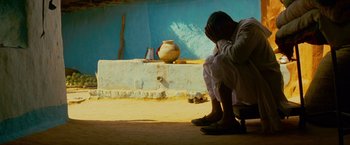 Movie still from “The Darjeeling Limited” (2007), directed by Wes Anderson – A man sitting on the ground in front of a pot; Medium shot, High angle