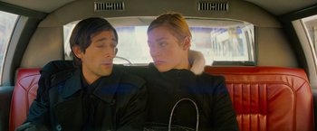 Movie still from “The Darjeeling Limited” (2007), directed by Wes Anderson – A man and a woman sitting in the back seat of a car; Medium shot, Over the shoulder angle