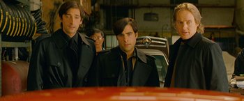 Movie still from “The Darjeeling Limited” (2007), directed by Wes Anderson – A man in a black jacket standing next to another man in a black jacket; Medium shot, Low angle