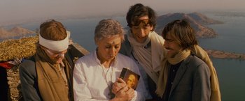 Movie still from “The Darjeeling Limited” (2007), directed by Wes Anderson – A woman is holding a book while two other people look on; Medium shot, High angle