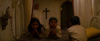 Movie still from “The Darjeeling Limited” (2007), directed by Wes Anderson – Two young children are praying in front of a cross; Medium shot, Low angle