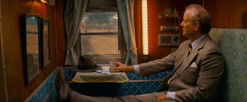 Movie still from “The Darjeeling Limited” (2007), directed by Wes Anderson – A man sitting at a table in front of a window; Medium shot, High angle